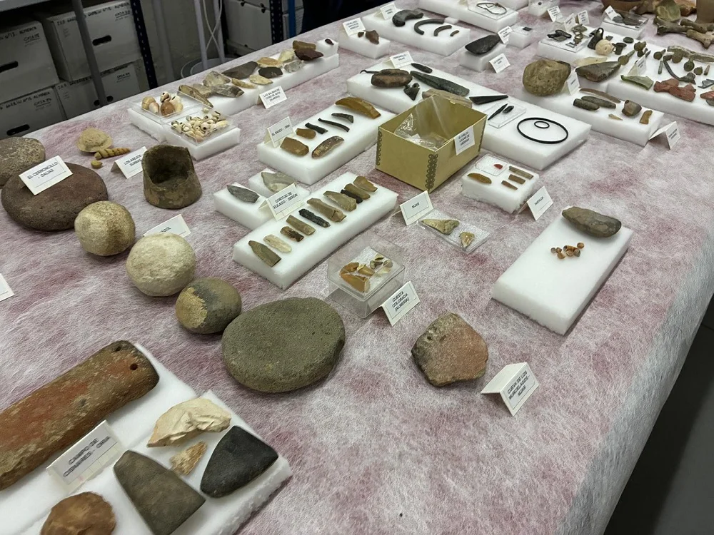 Detalle de piezas de piedra, herramientas, adornos y otros objetos arqueológicos dispuestos sobre una mesa.