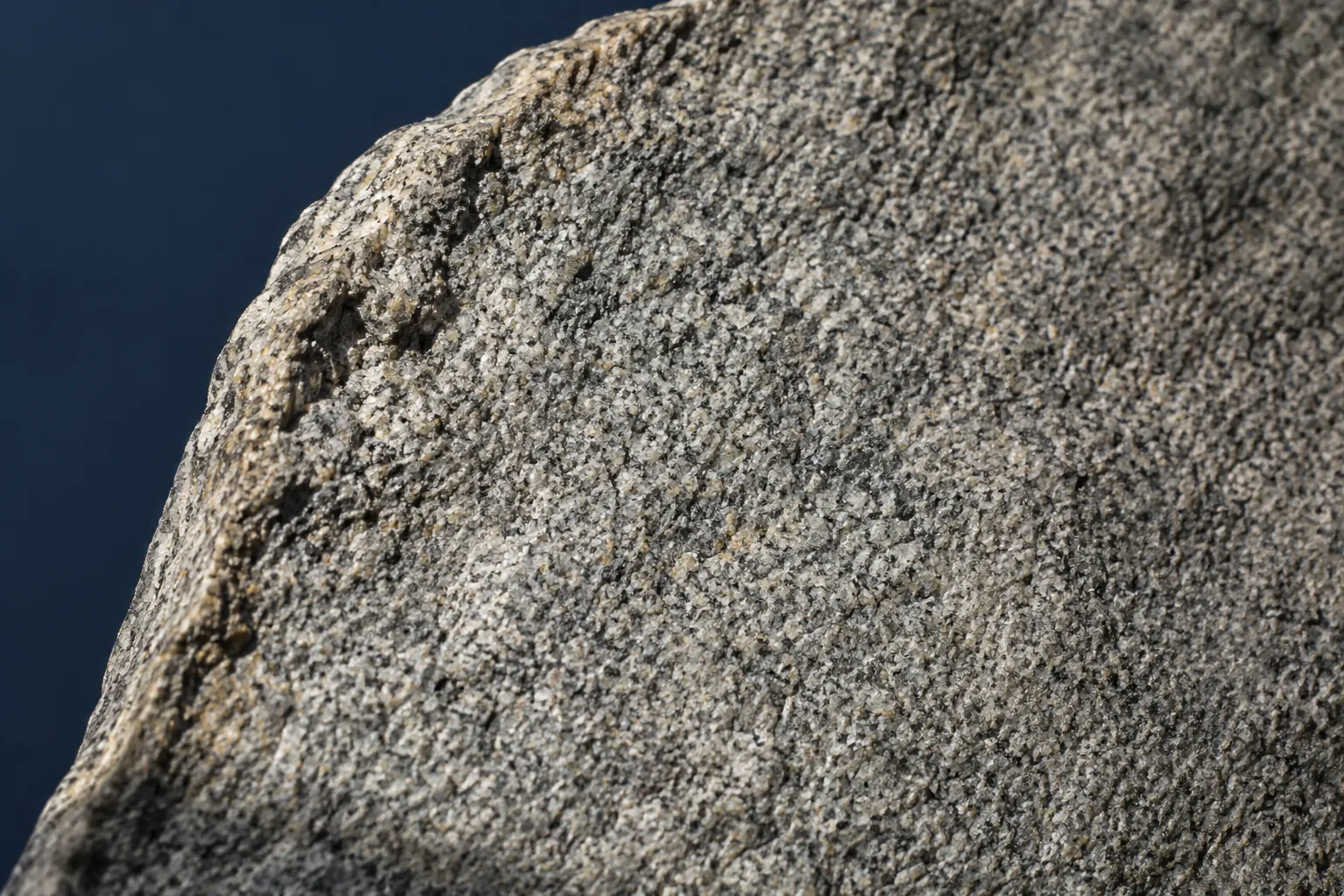Detalle oblicuo de una superficie de granito sin grabados sobre fondo azul, ilustración generada con IA.